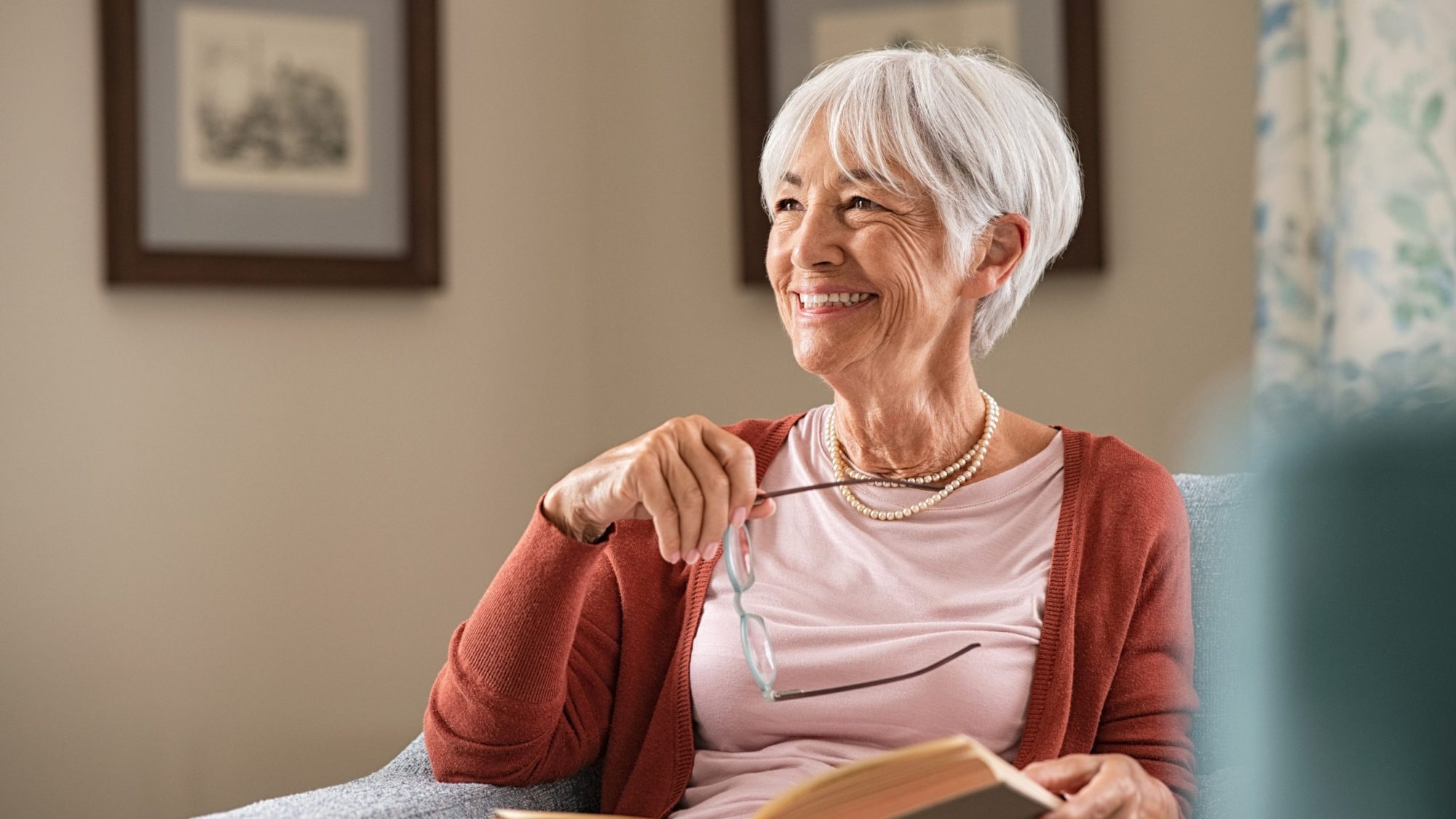 An older woman happily looking to her right with an open book in her lap.