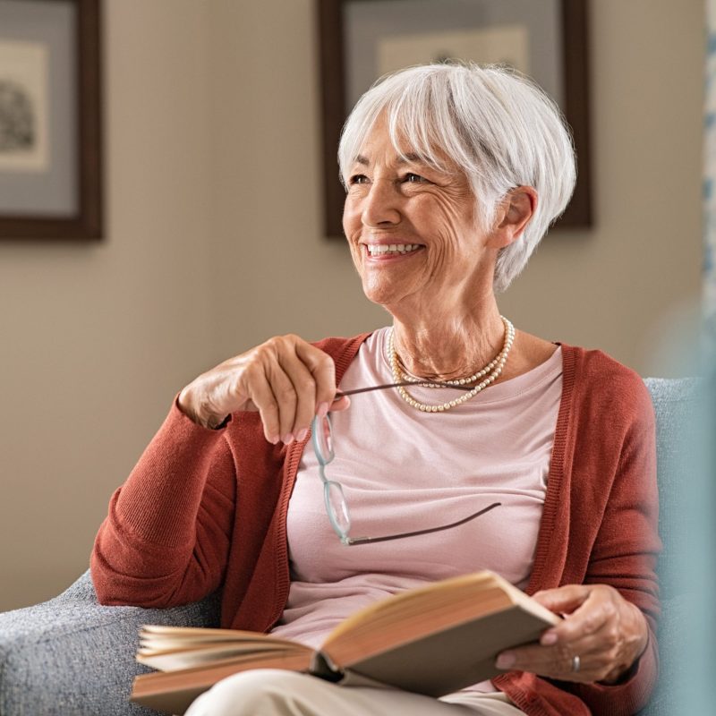 An older woman happily looking to her right with an open book in her lap.
