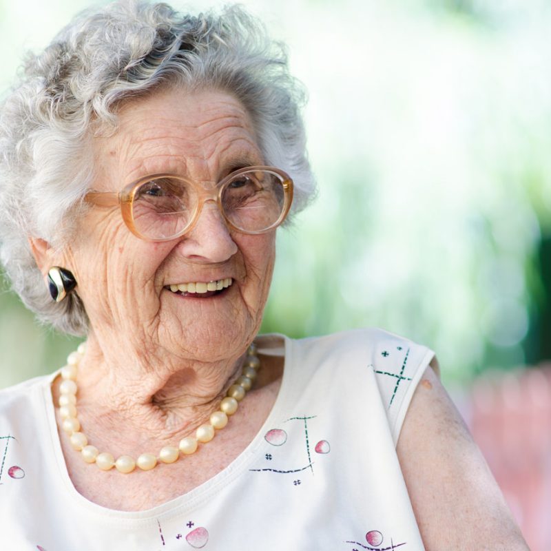 An older woman with short grey hair and brown glasses laughing and looking to her left