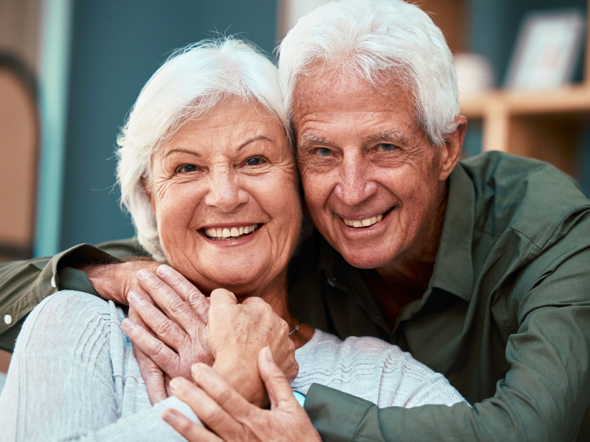 An elderly couple happily hugging and looking at the camera