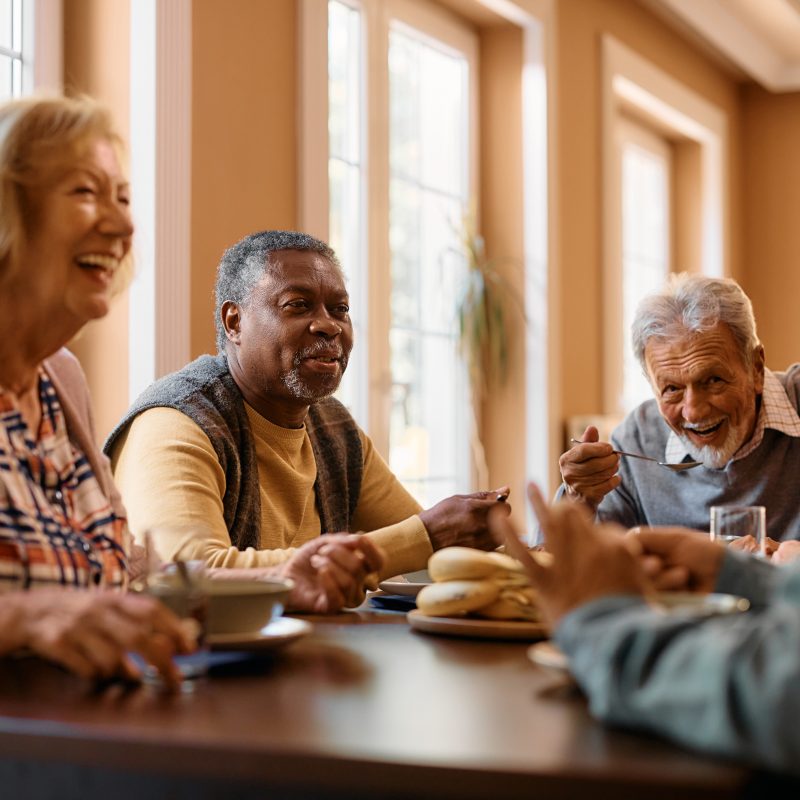 A group of older men and women laughing and sitting around a table together.