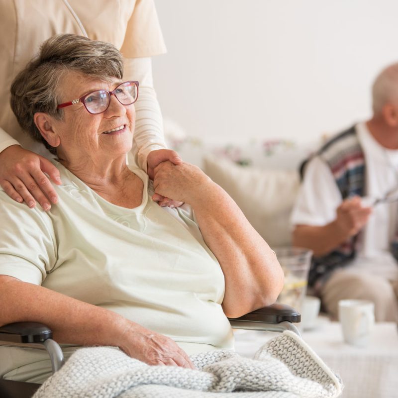 An older woman in a wheeling happily holding the hand of an aide