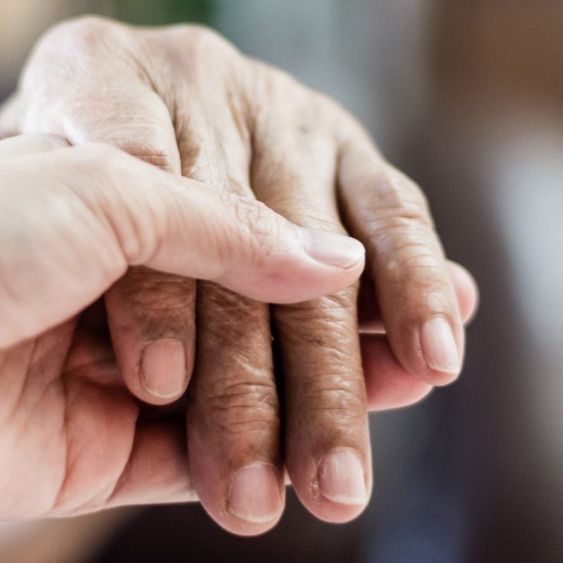 Young white female hand holding an older man of color's hand.
