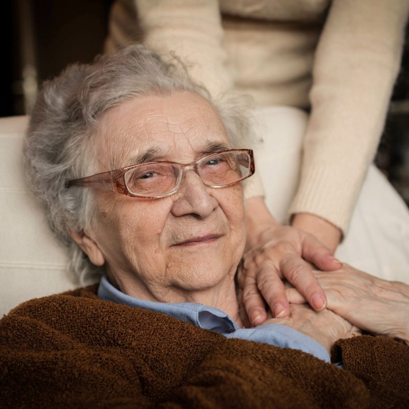 A woman laying in bed holding the hand of her caretaker