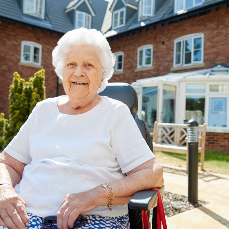 A happy older woman sitting in a wheelchair outside on a sunny day