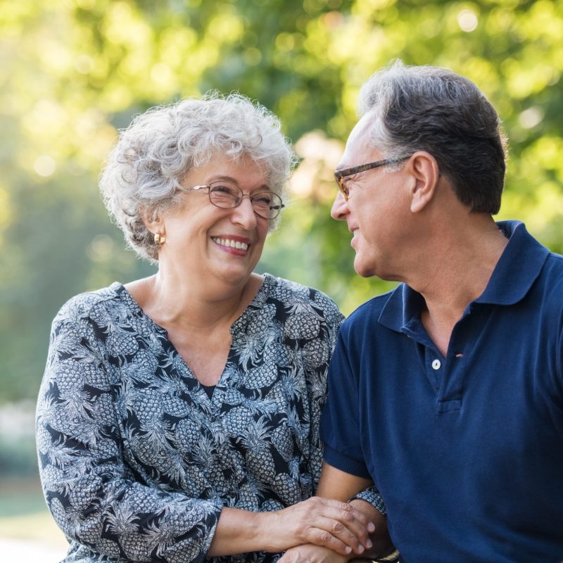 An older couple happily smiling at each other outside