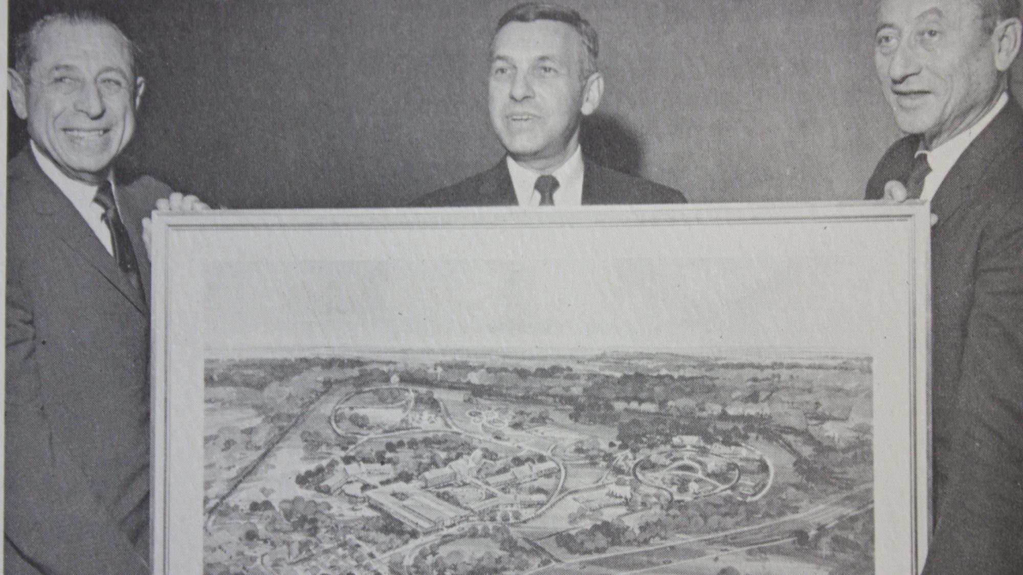 Three men holding a rendering of the Campus of Care